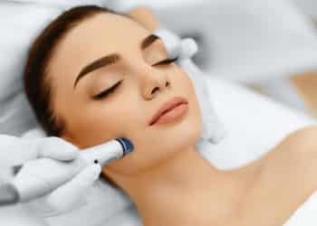 woman laying down as med spa professional performs microdermabrasion on her face using handheld device